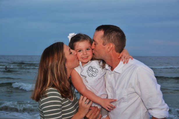 mom-dad-kissing-daughter-on-beach